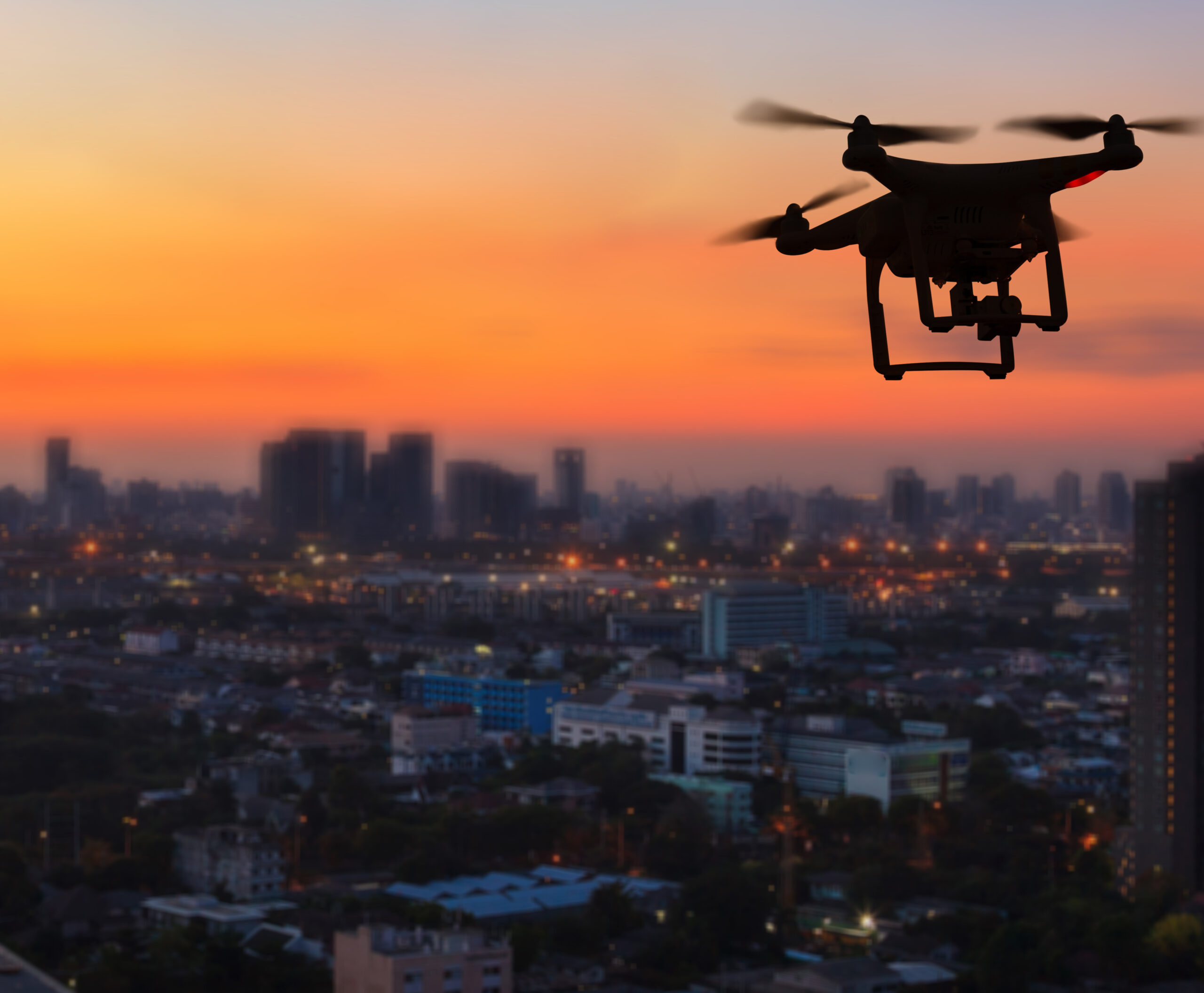 Silhouette of drone flying above city at sunset