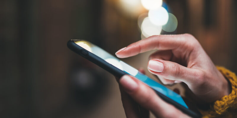 Point finger on screen phone closeup, person texting text message, hipster touch blue screen on smartphone light night city, girls using in hands mobile phone close up, online wi-fi internet