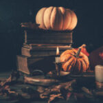 Still life for Halloween and Thanksgiving with old books, pumpkins and candle on dark background