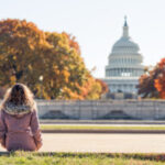 Young woman in coat sitting looking at view of United States Capital