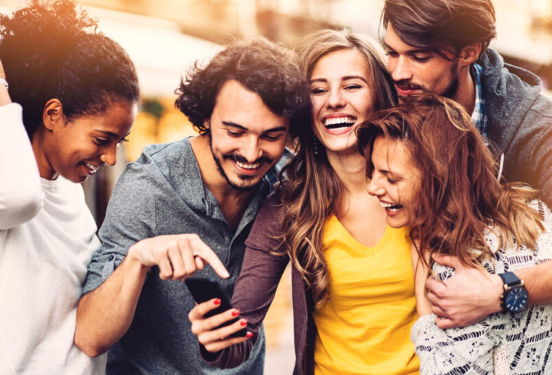 Five people laughing together holding phone