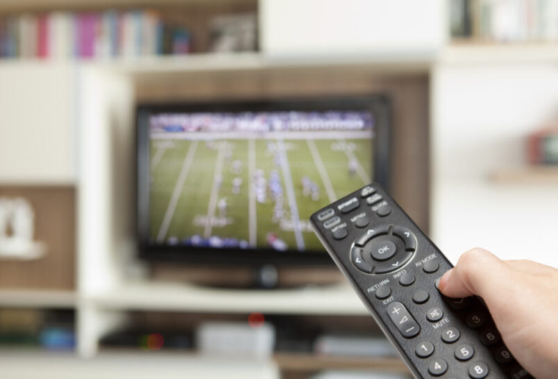 tv with american football on and a hand holding a remote