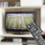 tv with american football on and a hand holding a remote