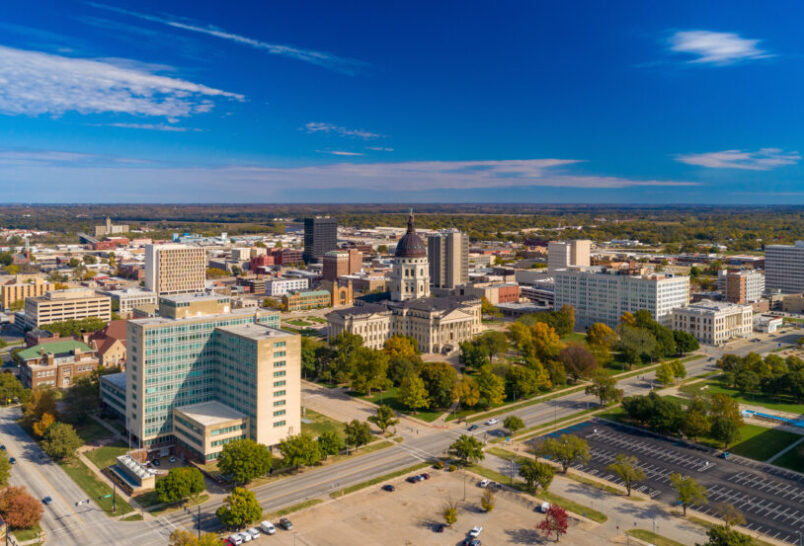 Downtown Topeka aerial skyline view with the Kansas State Capitol building in the center, and a blue sky with clouds in the background.
